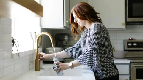 Getty Images Women with red hair fills a bottle with water from the tap