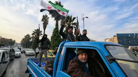 AFP Syrian rebel fighters celebrate and hold up the Free Syria flag in Damascus after President Bashar al-Assad reportedly fled abroad (8 December 2024)