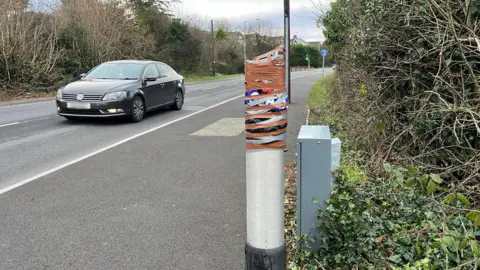 BBC A stretch of the A4102 in Merthyr Tydfil. It appears the camera - in  layby -  has been broken off and the post has been taped up. Photo shows a black VW car driving past.