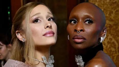 Reuters Ariana Grande and Cynthia Erivo facing each other and both looking sideways in the same direction, wearing jewelled necklaces and earrings at the Australian premiere of Wicked in November.