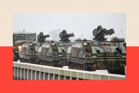 Getty Images Taiwanese armoured vehicles roll down a street in Kinmen in May. There are three tanks and the sky is grey.