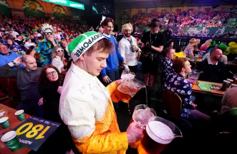 PA Media A man dressed in a beer glass costume holds four jugs of beer