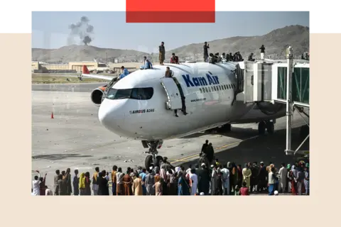 Getty Images People climb atop a plane as they wait at the Kabul airport, and crowd around, there is smoke in the background