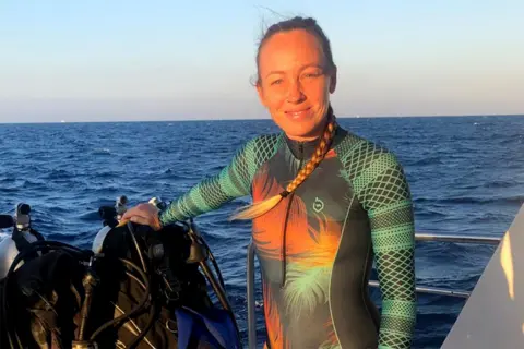 Hissora Gonzalez Hissora Gonzalez standing on a boat at sea in a green and orange wetsuit.