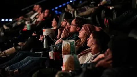 Reuters People in a row in a multiplex cinema. They are looking at the screen with popcorn and soft drinks