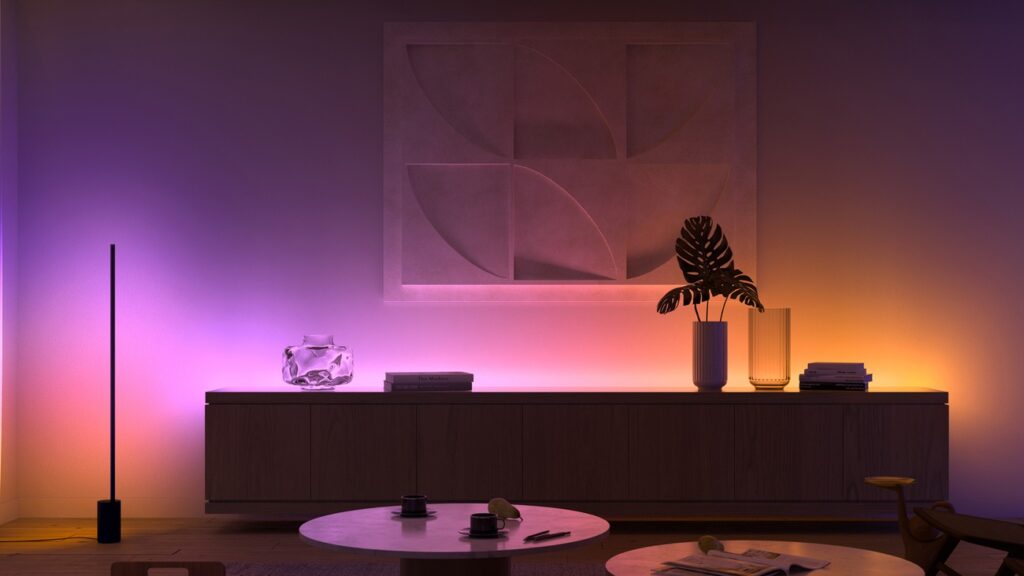 A modern living room illuminated by Philips Hue smart lighting, displaying a gradient of warm and cool colors on the walls and furniture